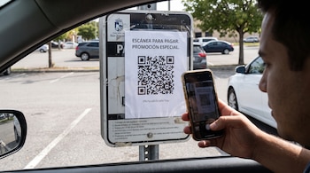 Un hombre dentro de un automóvil apunta con su teléfono móvil hacia un código QR pegado en una señal de estacionamiento.