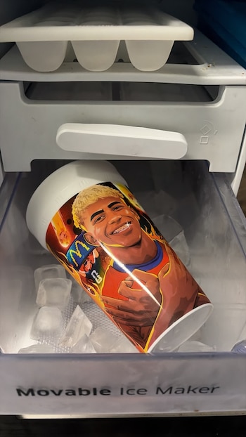 Vaso con ilustración de un hombre rubio sonriente, entre cubos de hielo en un cajón de congelador. Se lee "Movable Ice Maker"