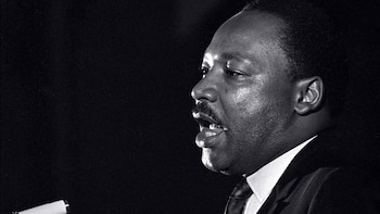 Primer plano en blanco y negro de Martin Luther King Jr. de perfil, con la boca ligeramente abierta, hablando en un micrófono con fondo oscuro