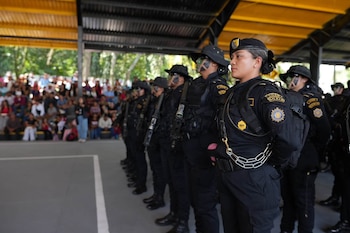 Fila de mujeres uniformadas de negro, algunas con boinas, otras con sombreros, fusiles, equipamiento táctico, parches SGAIA y maquillaje de camuflaje