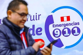 Hombre borroso con gafas y chaqueta oscura sostiene un teléfono inteligente, frente a un logotipo circular azul del 911 con bandera de Perú
