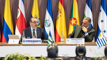 Dos hombres en traje sentados ante carteles identificativos de la CAF y Uruguay, con banderas nacionales de fondo