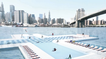 Vista aérea de una piscina flotante blanca en el East River de Nueva York, con personas nadando y tomando el sol. Al fondo, rascacielos y el Puente de Brooklyn