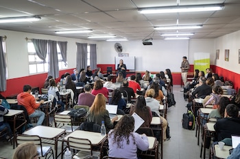 Decenas de personas sentadas en pupitres individuales dentro de un aula con computadoras portátiles y cuadernos