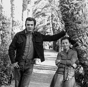 Fotografía en blanco y negro de un hombre y una mujer de pie junto al tronco de una palmera en un camino con vegetación
