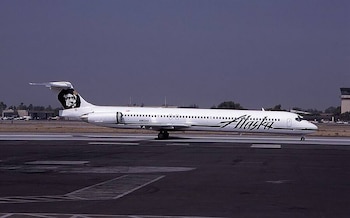 Un avión de pasajeros blanco con el logotipo de Alaska Airlines en la cola, sobre una pista de asfalto de un aeropuerto