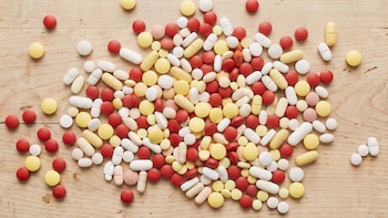 Varias píldoras y tabletas de colores rojo, amarillo, blanco y rosa, con formas redondas, ovaladas y alargadas, sobre una superficie de madera