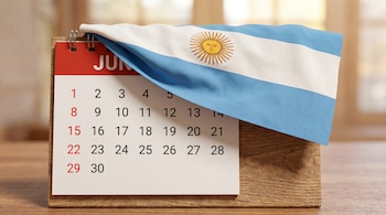 Calendario de sobremesa para junio sobre una base de madera, con una bandera argentina que lo cubre parcialmente desde arriba.