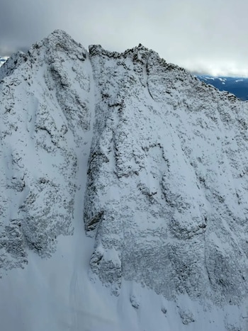 Vista aérea de una montaña rocosa y empinada cubierta de nieve y hielo bajo un cielo nublado
