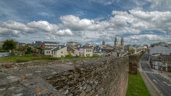 Vista panorámica de la muralla romana de Lugo desde su parte superior, con el casco histórico de la ciudad y la catedral al fondo bajo un cielo nublado.