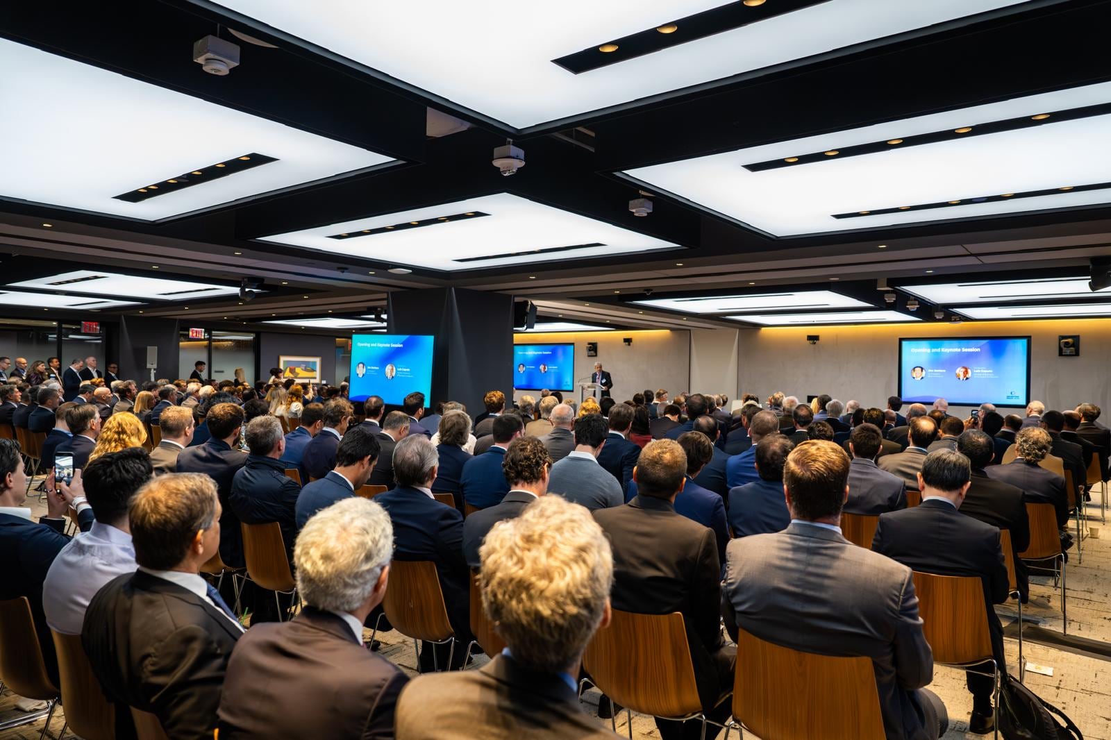 Asistentes escuchan atentamente durante la sesión de apertura de la Semana Argentina, donde un orador se dirige a la audiencia frente a pantallas con información del evento.