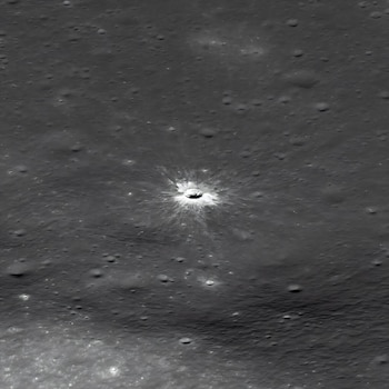 Fotografía en blanco y negro de un cráter de impacto central con destellos brillantes sobre un terreno gris cubierto de pequeños cráteres