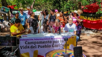 Un grupo de personas se sienta ante una mesa con una pancarta sobre la solidaridad con el Pueblo Garífuna