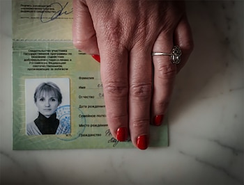 Una mano sobre un documento de identidad abierto con una fotografía en blanco y negro y texto en alfabeto cirílico