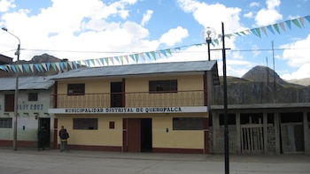 Edificio amarillo de dos pisos con la frase Municipalidad Distrital de Queropalca, calle con banderines y montañas de fondo