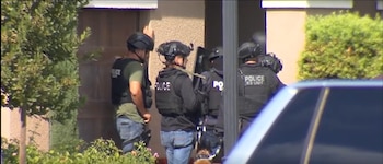 Varios agentes de policía equipados con chalecos tácticos y cascos permanecen junto a la puerta de una vivienda