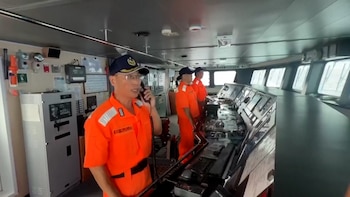 Un oficial de la Guardia Costera taiwanesa, con uniforme naranja y gorra, habla por un teléfono fijo en el puente de mando de un barco, junto a otros dos oficiales