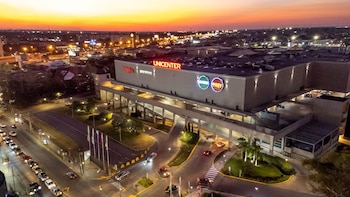 Vista aérea del edificio de Unicenter con carteles luminosos, rampas de estacionamiento, vehículos en las vías de acceso y cielo al atardecer