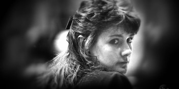 Mujer de perfil con cabello rizado y un pasador negro en la parte posterior, mirando de reojo sobre su hombro derecho, en una fotografía en blanco y negro