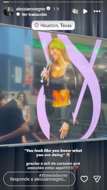 Alessia Rovegno, de cabello castaño y top negro, sonríe mientras sostiene un micrófono. Al fondo, una pantalla muestra el logo de Victoria's Secret