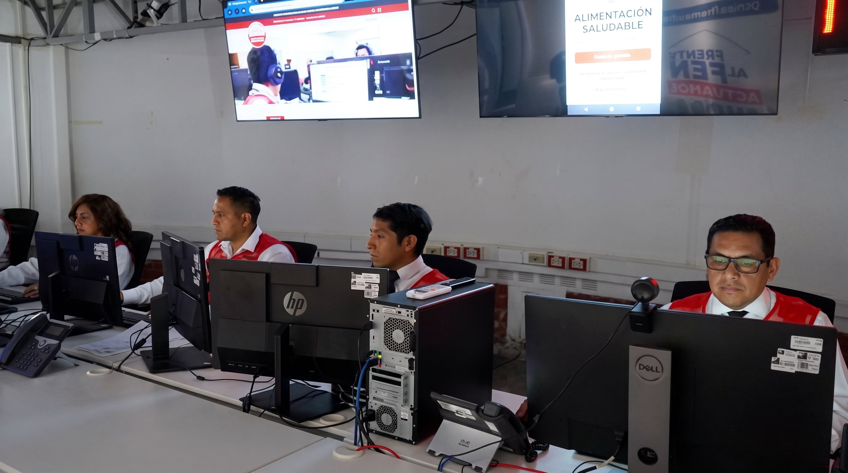 Un grupo de operadores atiende computadoras de escritorio en una sala equipada con pantallas institucionales colgadas en la pared. (Imagen Ilustrativa Infobae)