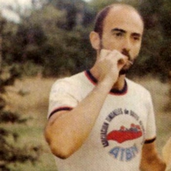 Primer plano de Indio Solari, un hombre con barba y calvicie incipiente, usando una camiseta blanca con logo, llevándose la mano a la boca