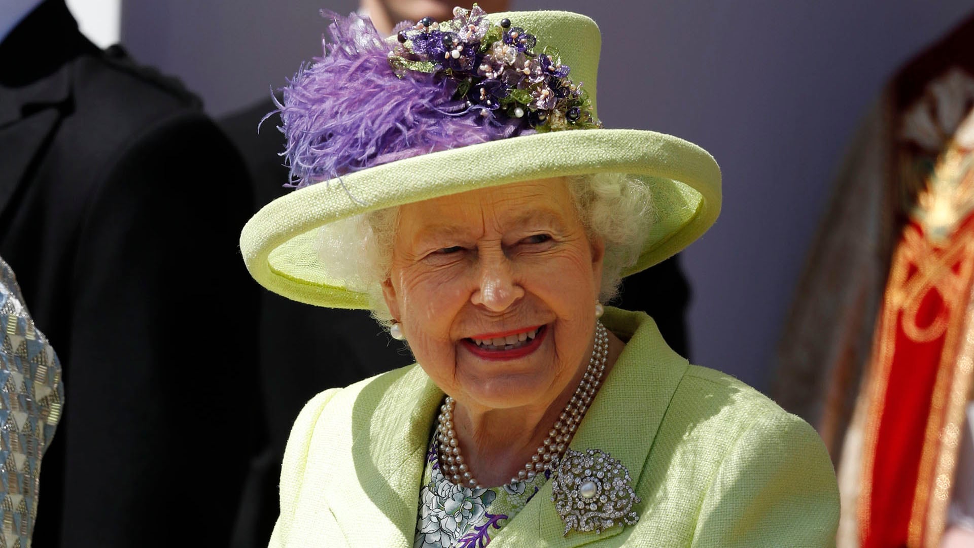 Abrigo verde claro y sombrero decorado con plumas y flores violetas, más collar triple de perlas y broche plateado (AFP)