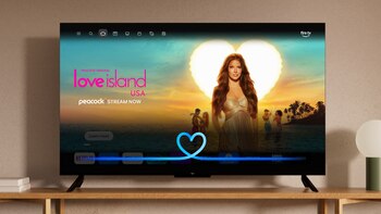 Televisor negro en mueble de madera con pantalla encendida; interfaz de Fire TV, anuncio de "Love Island USA", logos de plataformas de streaming