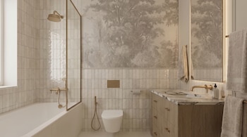 Vista completa de un baño moderno con azulejos verticales claros, bañera blanca, ducha con grifería dorada, inodoro suspendido y tocador con mármol. Una pared tiene papel tapiz de bosque en gris.