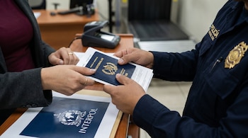 Manos femeninas entregan un pasaporte guatemalteco y documentos a un agente de la Policía Nacional Civil, que viste uniforme azul marino con insignia y tiene una carpeta de INTERPOL.
