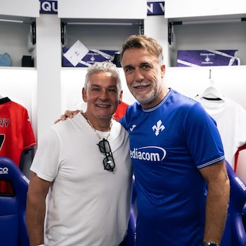 Roberto Baggio con camiseta blanca y Gabriel Batistuta con camiseta azul sonríen abrazados dentro de un vestuario deportivo