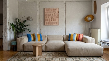 Un salón de diseño moderno con un sofá modular de pana beige, cojines a rayas coloridas, una mesa de centro de madera, un cuadro abstracto y plantas.