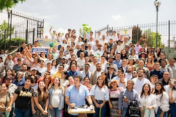 Gran multitud de personas sonrientes, hombres y mujeres de diversas edades, posando al aire libre con vallas, árboles y pancartas "Retalhuleu" y "San Marcos" al fondo