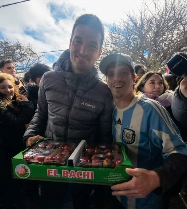 Lionel Scaloni sonríe junto a un aficionado que le entrega un cajón de frutillas como regalo en Pujato, provincia de Santa Fe