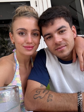 Una mujer con top de tejido colorido y un hombre con camiseta blanca y azul posan juntos en primer plano frente a la cámara