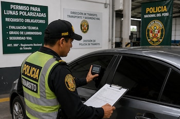 Un policía de tránsito mide la opacidad del vidrio de un automóvil con un dispositivo digital mientras sostiene una planilla de peritaje
