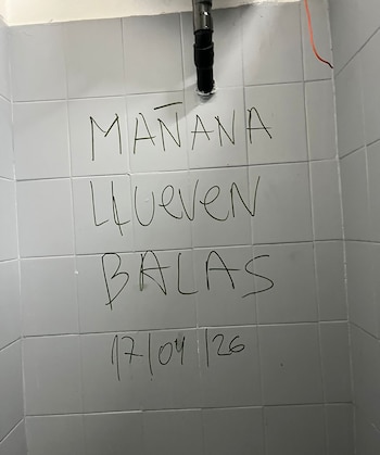 Grafiti en marcador negro sobre azulejos blancos, que dice "MAÑANA LLUEVEN BALAS" y la fecha "17/04/26" escrito en una pared de un baño
