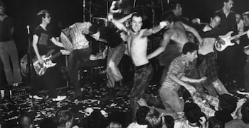 Fotografía en blanco y negro de un grupo de personas bailando y tocando la guitarra en un escenario durante un concierto
