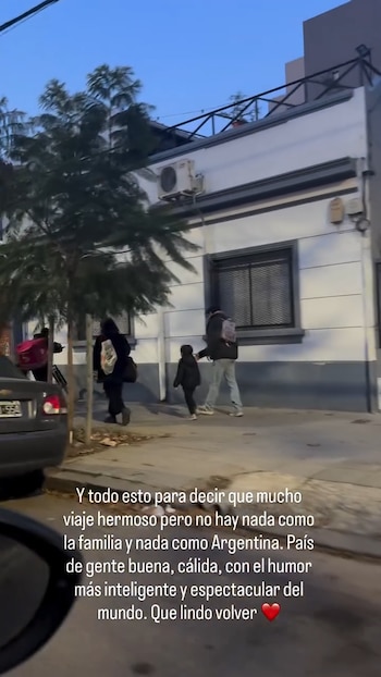 Varias personas borrosas caminan por una acera de noche, cerca de un coche oscuro y frente a un edificio con árboles