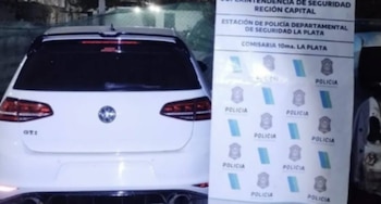 Parte trasera de un auto blanco Volkswagen Golf GTI, con cuatro tubos de escape, junto a un cartel de la Policía de la Comisaría 10ma. La Plata