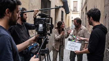 Un equipo de filmación graba a dos actores en un callejón estrecho con una cámara en posición vertical, un micrófono y una claqueta.