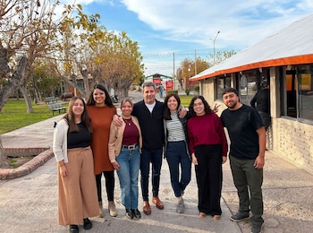 Siete personas, incluyendo a Sergio Uñac, posan sonrientes al aire libre. De fondo, árboles, un camino pavimentado y un edificio