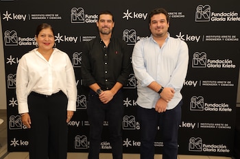 Una mujer y dos hombres posan de pie frente a un fondo negro con los logos del Key Institute y la Fundación Gloria Kriete