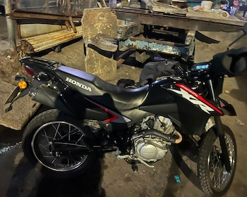 Una motocicleta negra marca Honda modelo XR está estacionada sobre el asfalto. Al fondo se observan escombros y restos de construcción