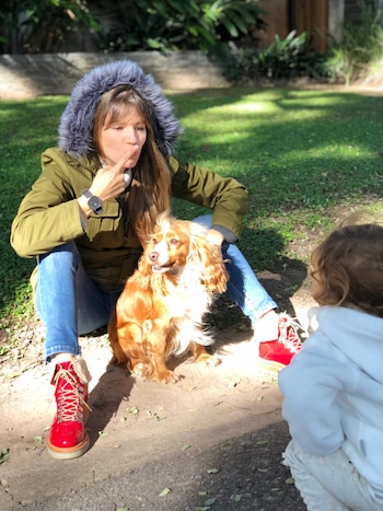 Mujer con chaqueta verde sentada con un perro cocker spaniel y un niño. La mujer hace un gesto divertido con la mano, el perro mira a un lado