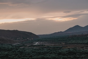 Montañas alrededor de un valle verde con vegetación y un pequeño río serpenteante bajo un cielo nublado