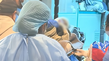 Personal médico con gorros y batas quirúrgicas atiende a un paciente recostado sobre una camilla en una sala de hospital