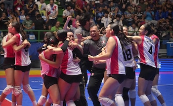 Jugadoras y entrenadores vestidores con uniforme deportivo rojo y blanco se abrazan y festejan en la cancha de voleibol