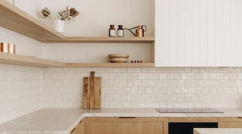 Rincón de cocina moderno con estantes flotantes de madera clara, encimera de mármol, backsplash de azulejos blancos y un horno integrado.