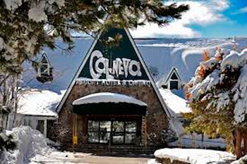 Vista exterior del Cal Neva Lodge cubierto de nieve en un día soleado. El letrero del resort es visible. Pinos nevados adornan el primer plano